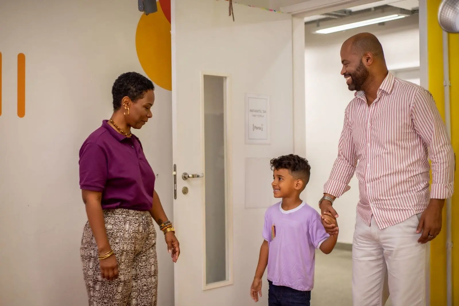 Um pai e uma professora conversam com um menino na escola.