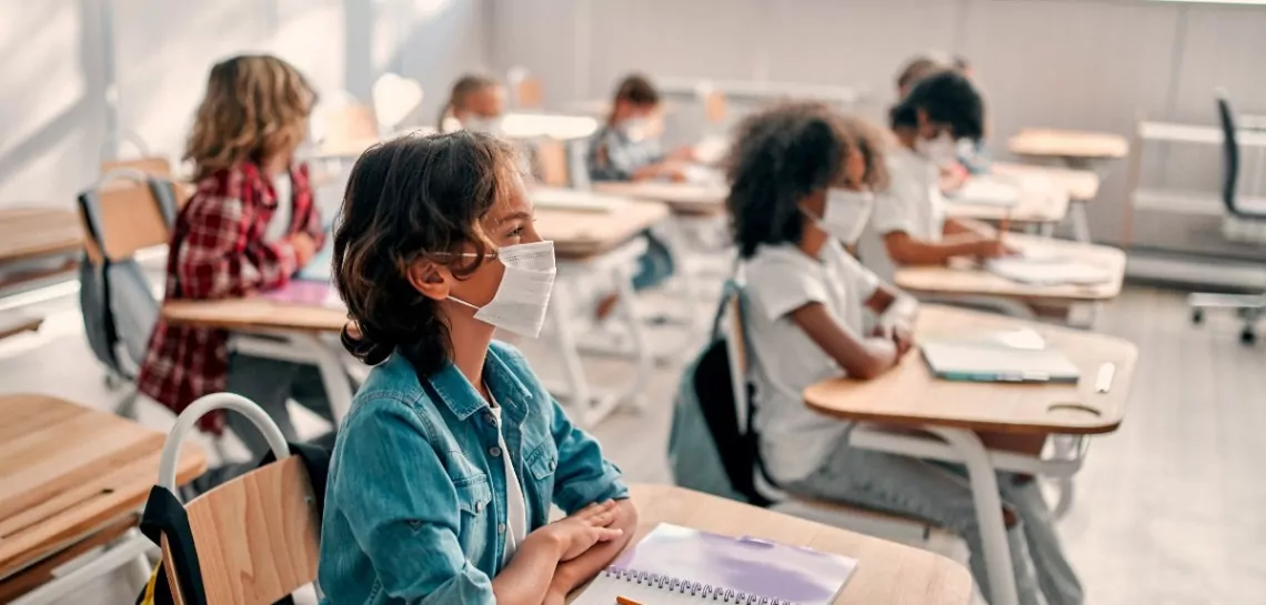 Alunos usando máscaras na sala de aula representando o ensino híbrido.
