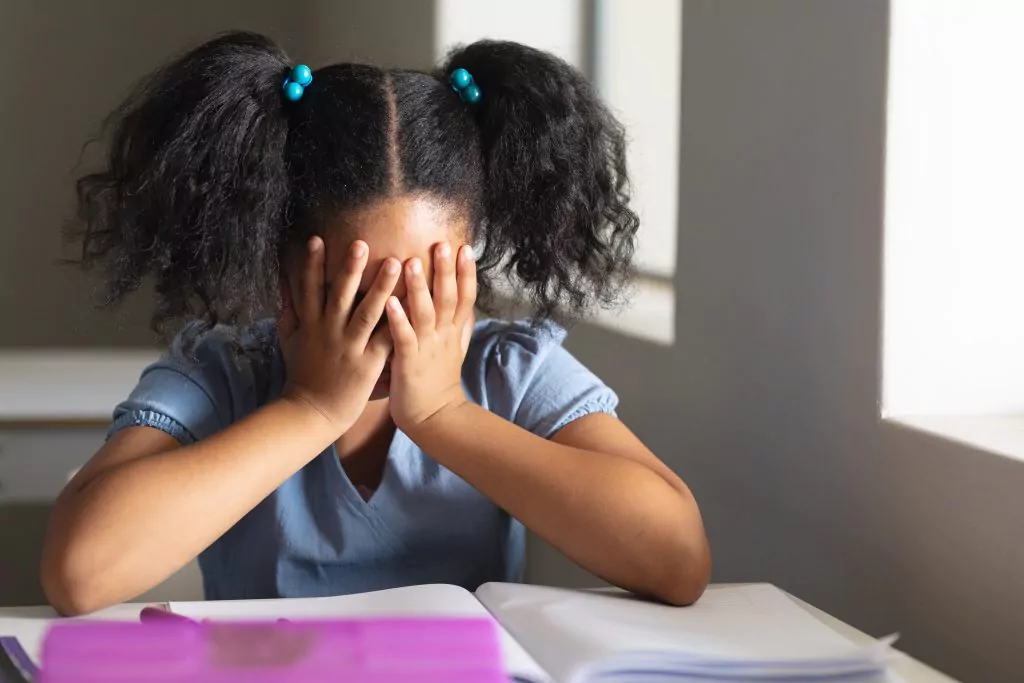 Criança negra com as mãos no rosto, em crise de ansiedade.